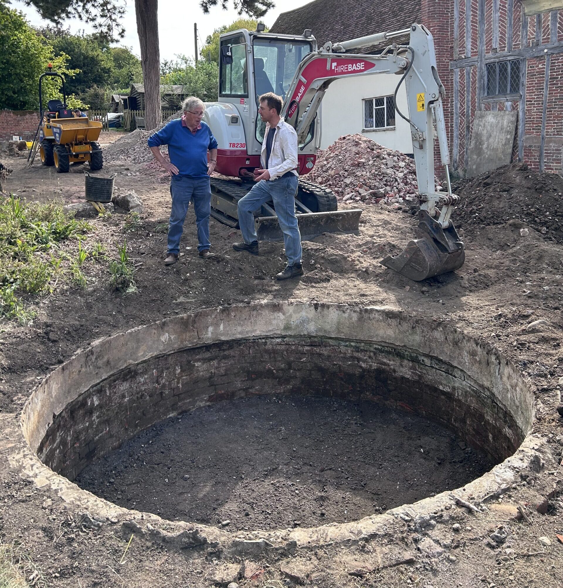 Dug out cistern with two men on other side of it and a digger behind them.